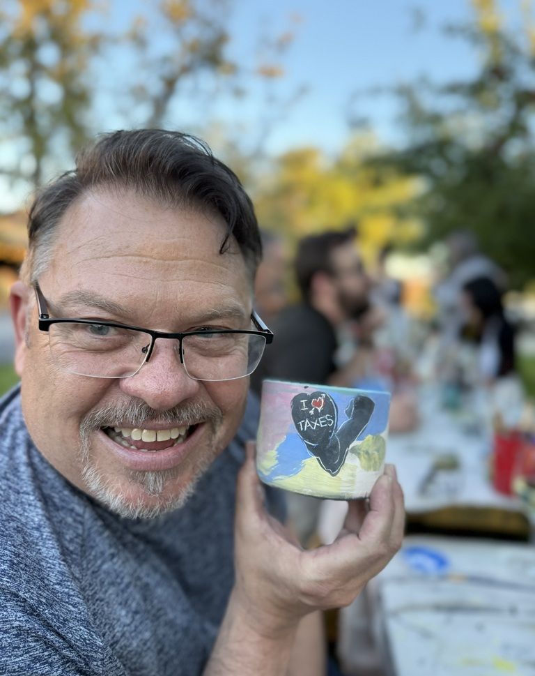 John Warekois holding up a handmade mug that says "I love taxes"
